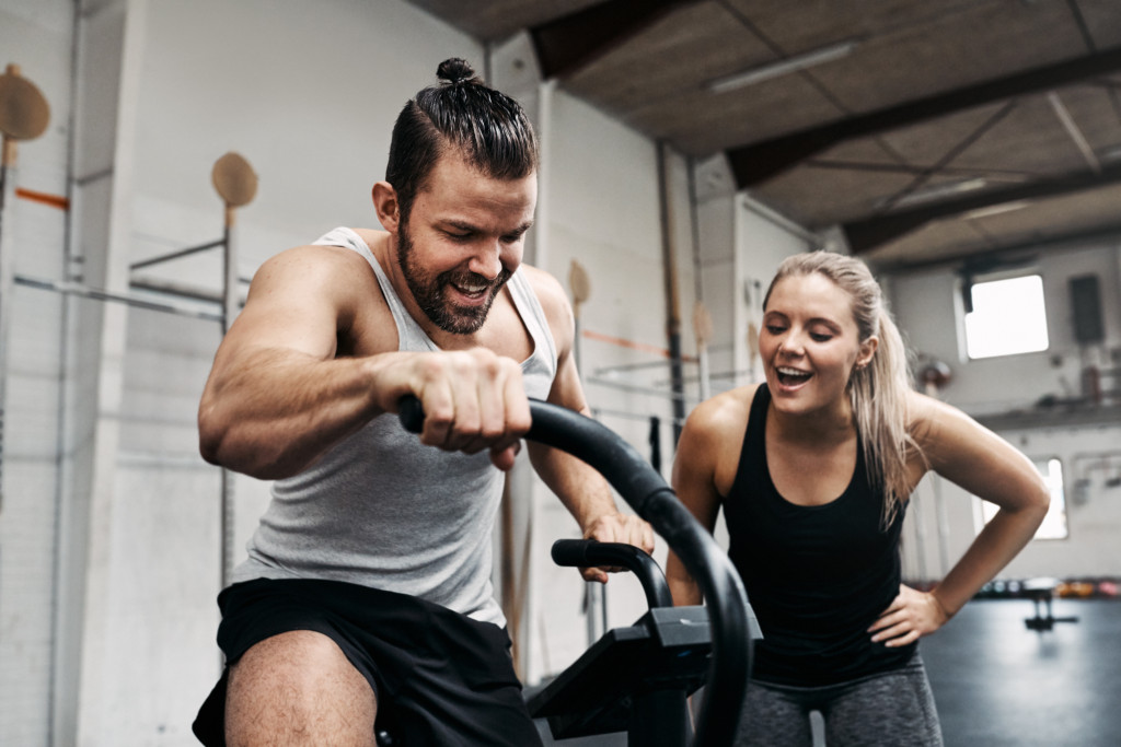 A woman encouraging her male friend who's riding a stationary bike