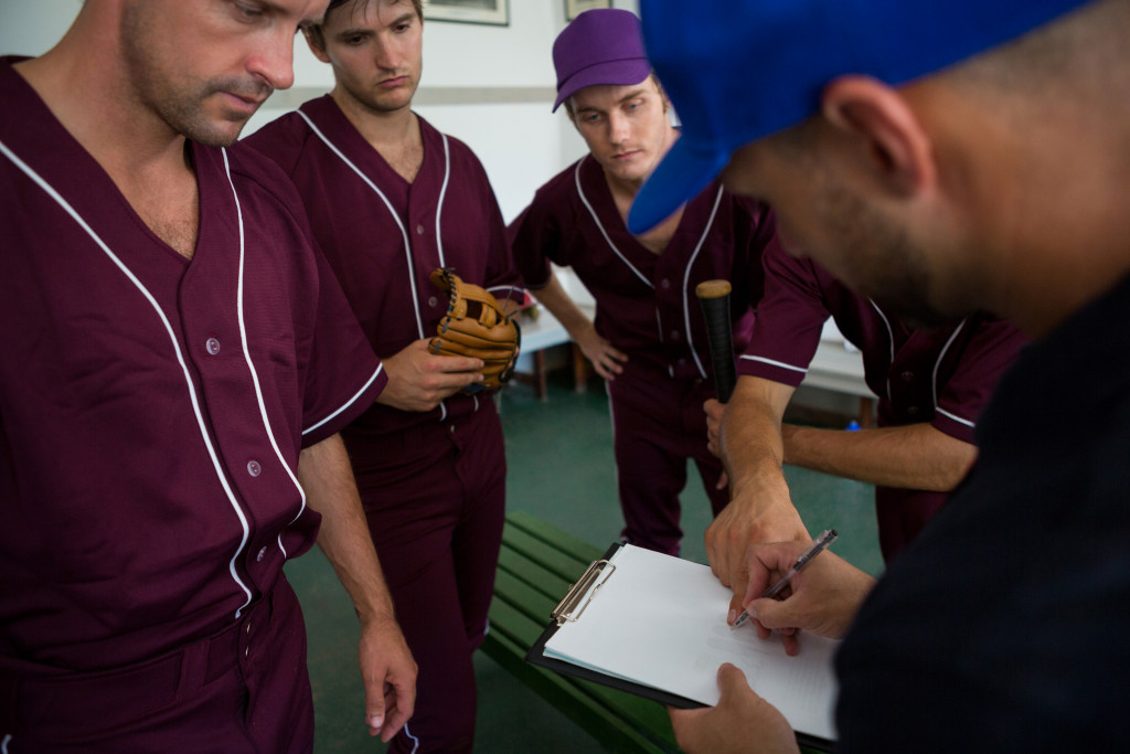 Baseball coach preparing the strategy for a game by writing it on paper with the players looking at him.