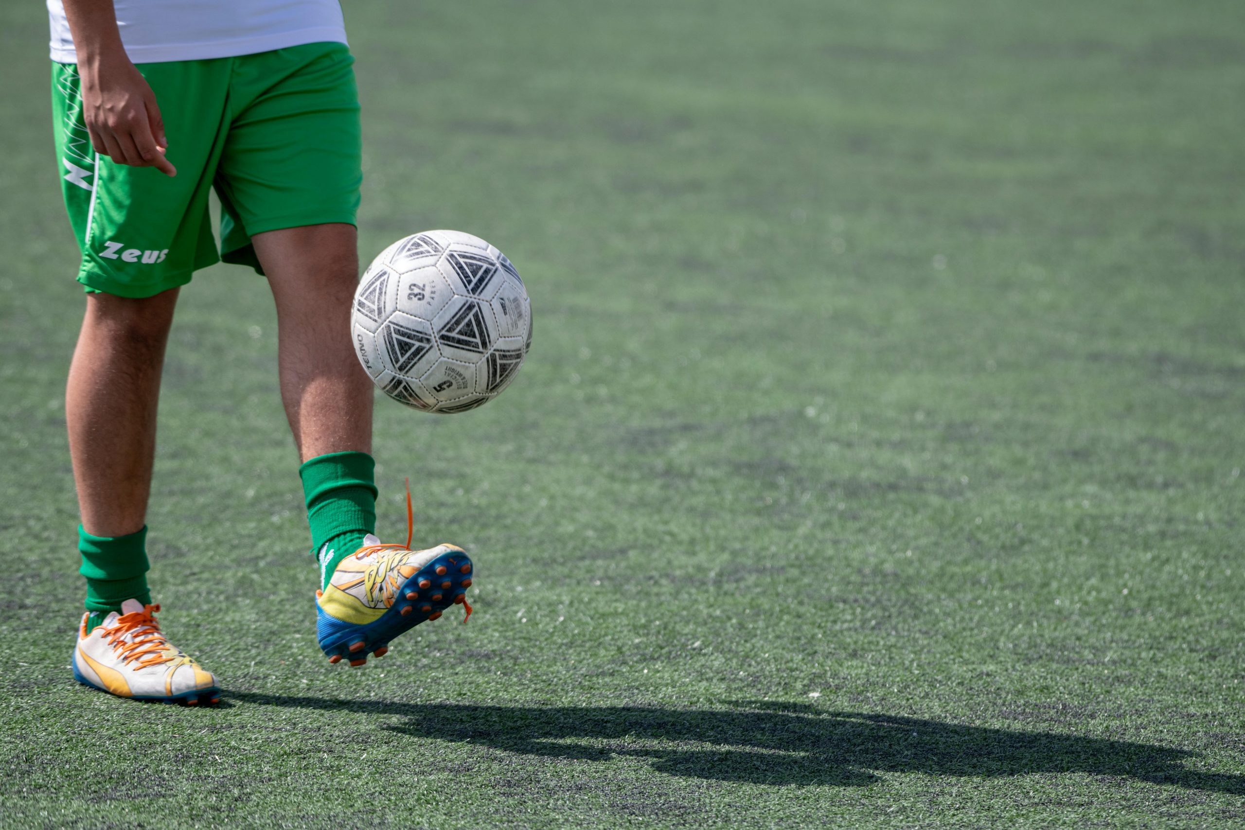 athlete wearing colorful cleats juggling a soccer ball on an outdoor field