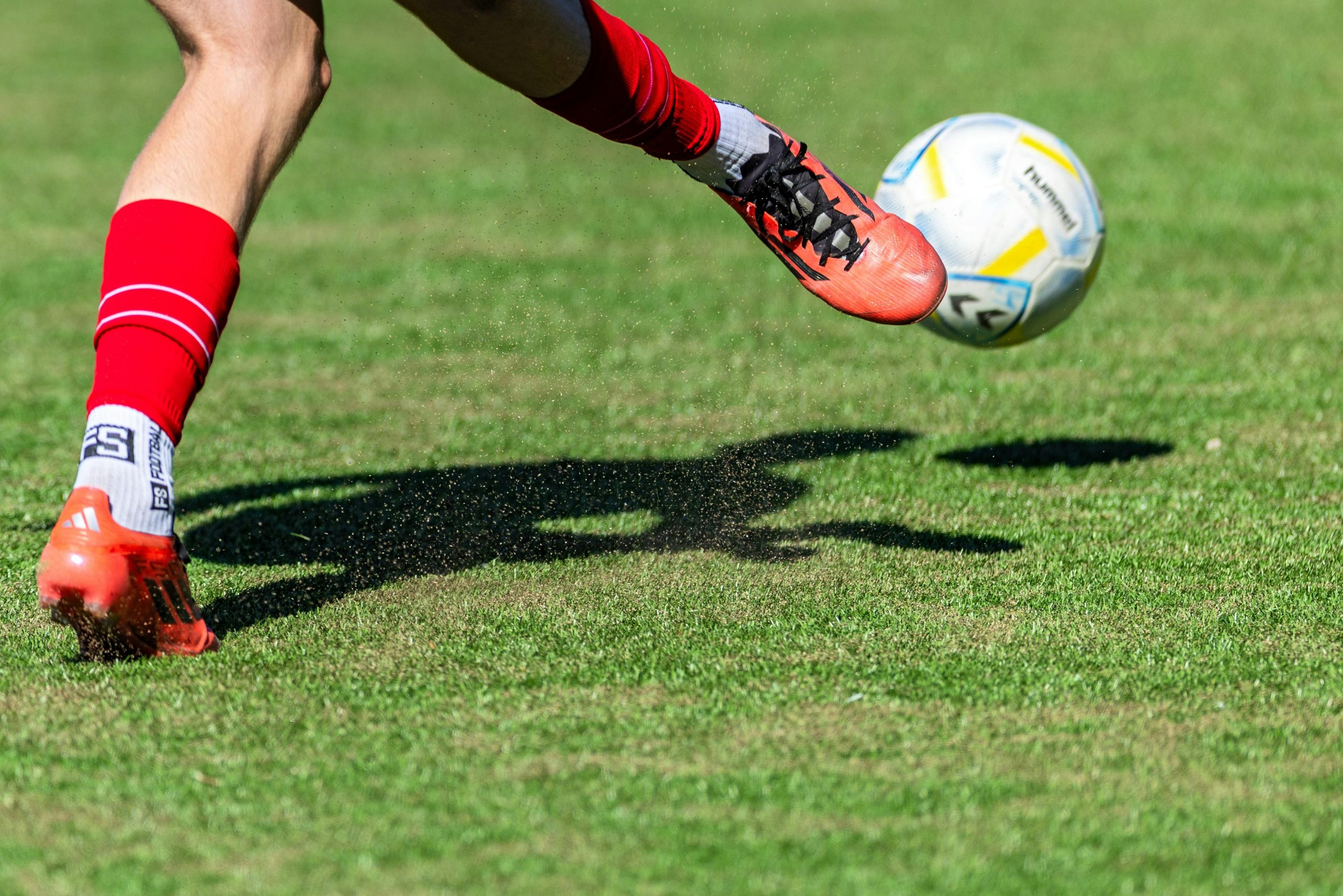 soccer player wearing red cleats kicking a ball on a grassy field