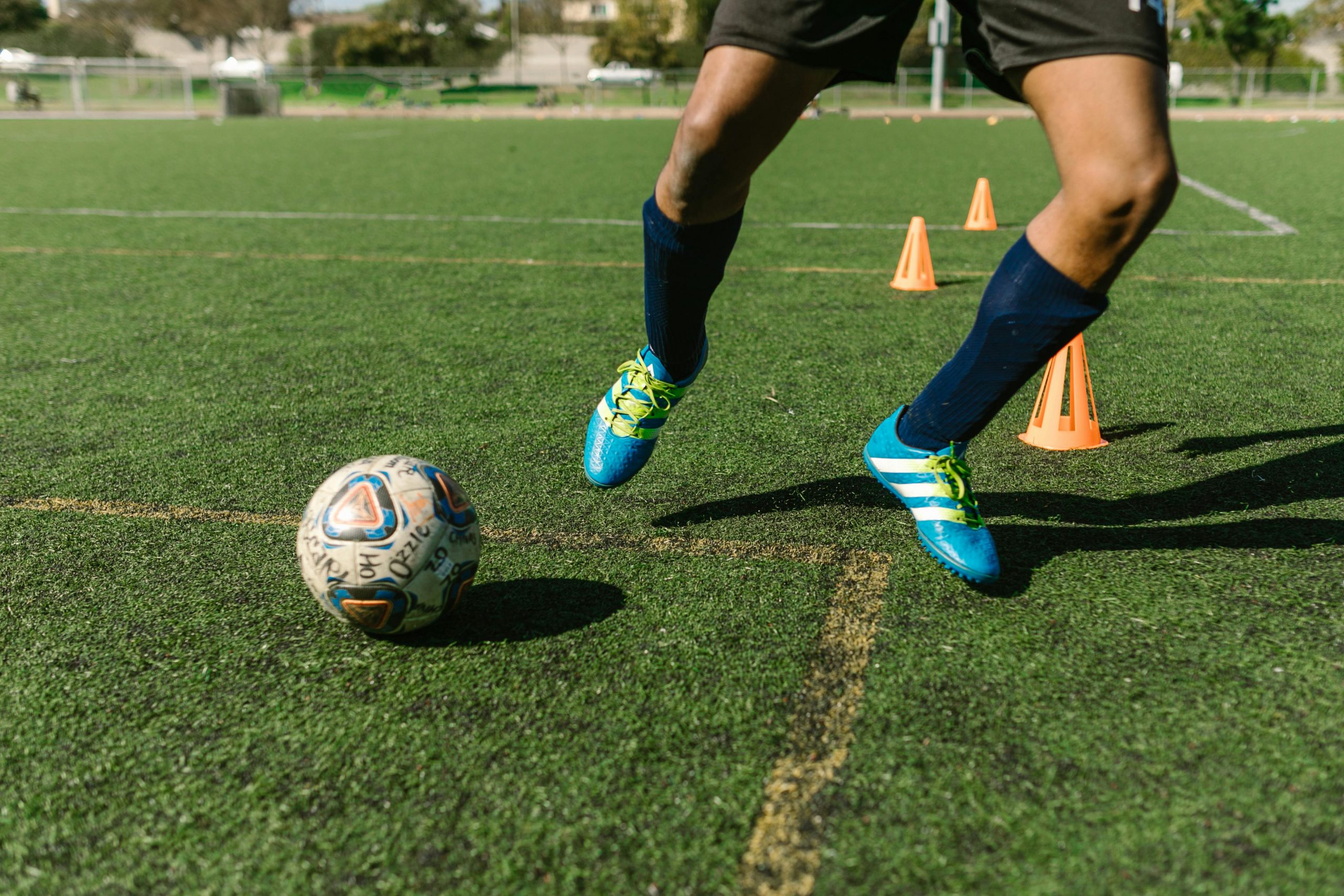 soccer player wearing blue cleats performing a kicking drill with small cones on an outdoor field